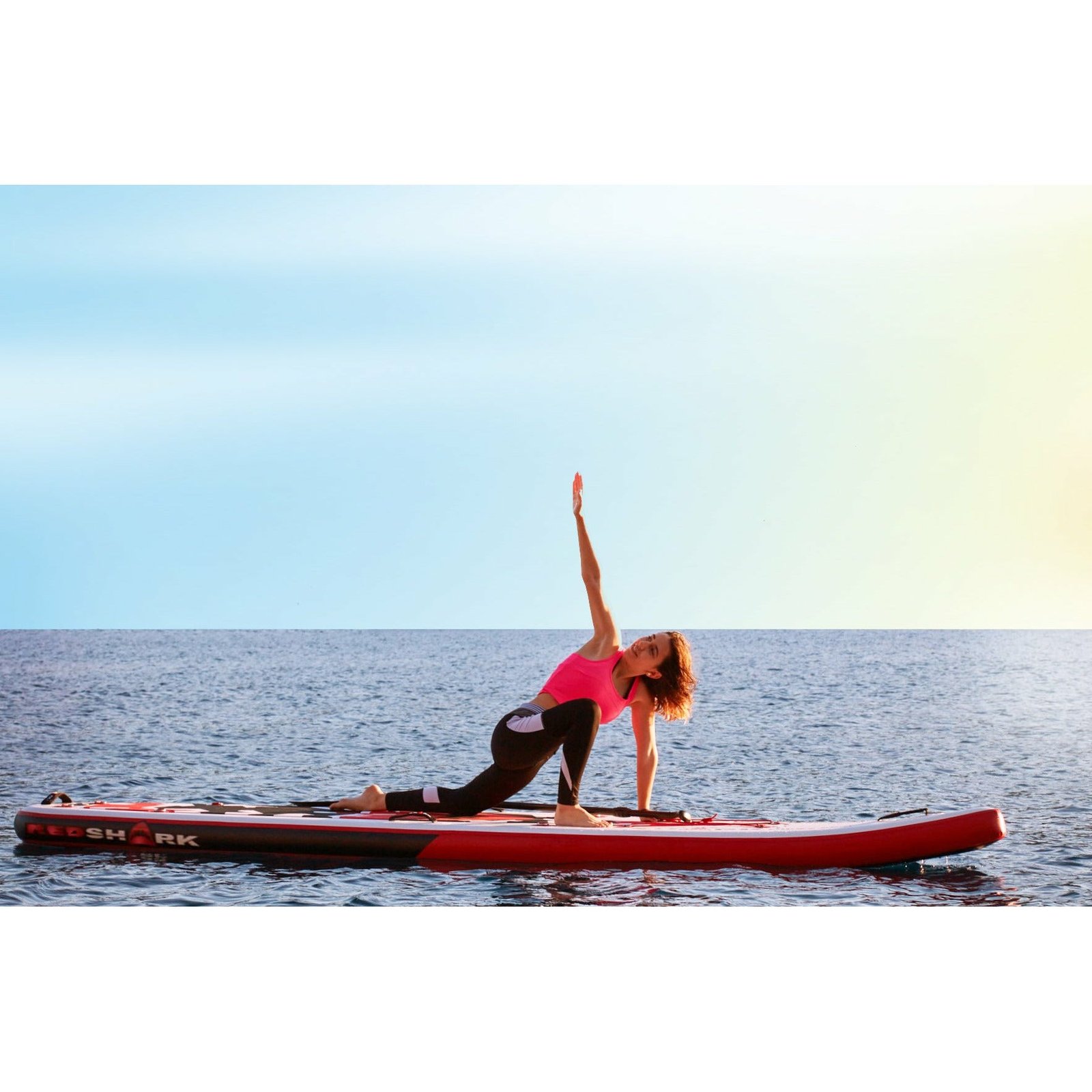 Vrouw doet een yogahouding op een Red Shark board op open water