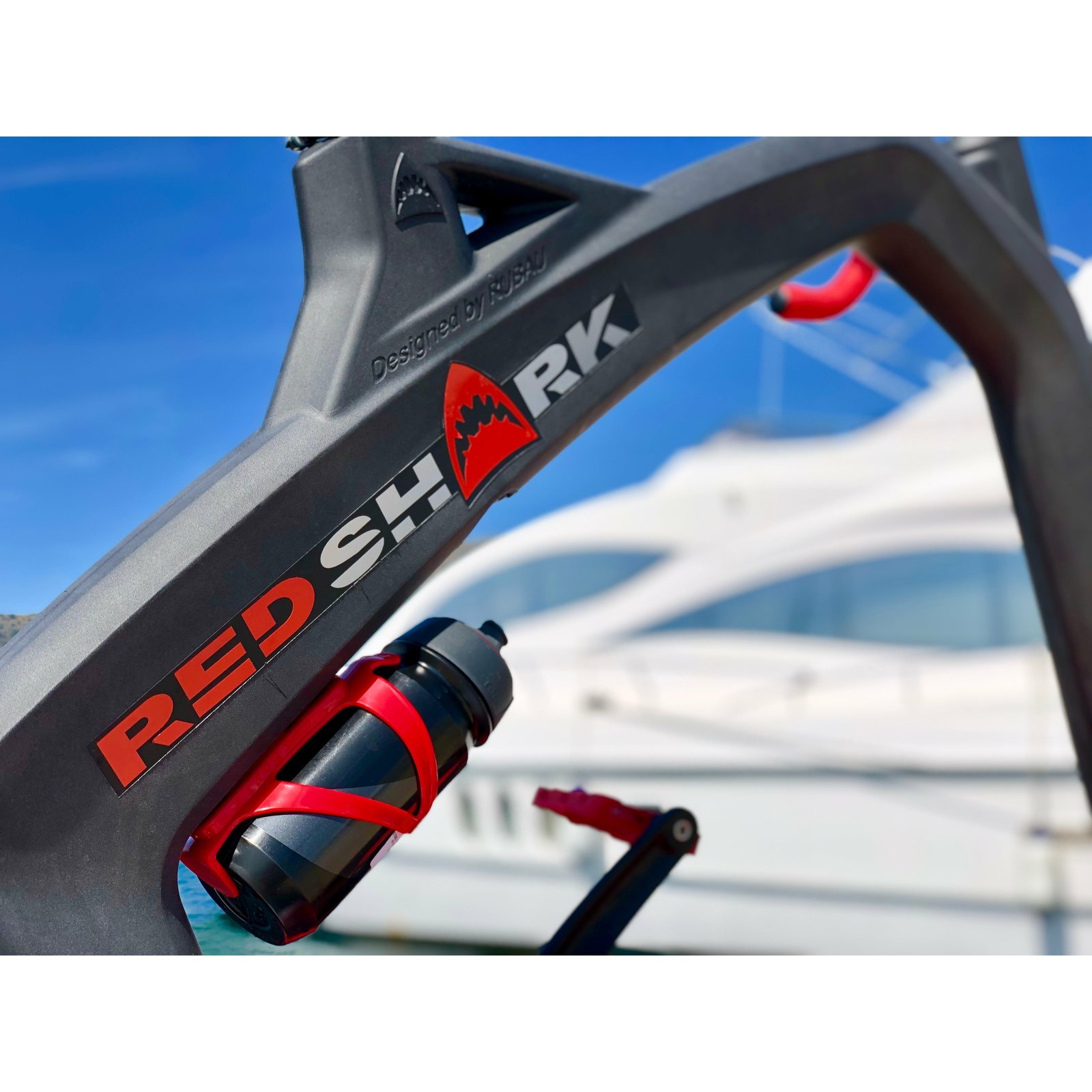 Close-up van het Red Shark frame met bidon, met een jacht in de haven op de achtergrond