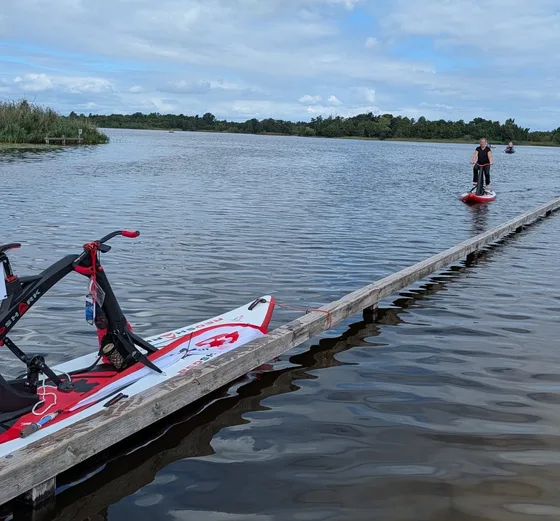 Vrouw komt aanvaren op een Red Shark langs een houten steiger op de Loosdrechtse Plassen, met op de voorgrond een tweede Red Shark op de steiger