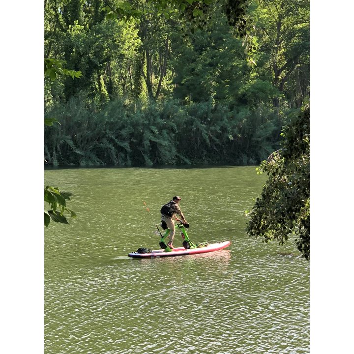 Rijder op een Red Shark Adventurer met hengel op een rustige rivier tussen groen